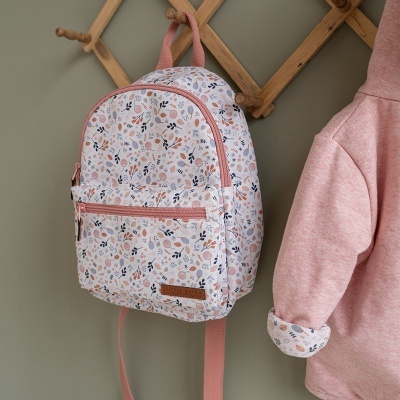 Mochila infantil floral com alças rosa pendurada num cabide ao lado de roupa rosa