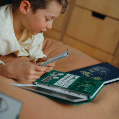 Menino deitado a ler com cadernos coloridos sobre cama em quarto com móveis de madeira clara