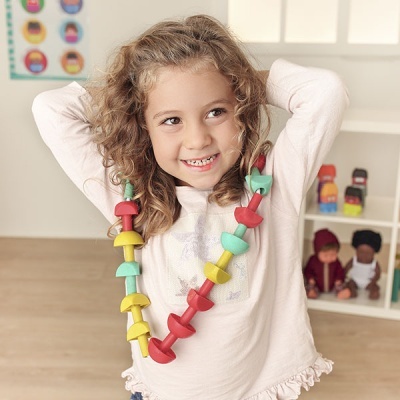 Criança com colar colorido a sorrir em ambiente interior com brinquedos ao fundo