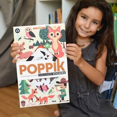 Menina com vestido cinza segurando poster de stickers Poppik com animais coloridos