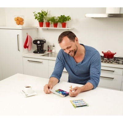 Homem numa cozinha branca a jogar xadrez colorido com chávena de café