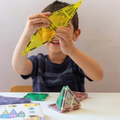 Criança com triângulo amarelo de plástico translúcido e outras formas geométricas coloridas na mesa