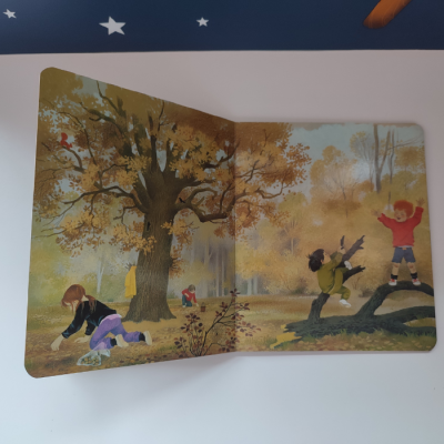 Livro infantil ilustrado aberto com crianças a brincar na natureza outonal