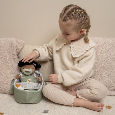 Criança com roupa de malha cremosa sentada com boneca de tecido castanha dentro de cesto verde de tecido