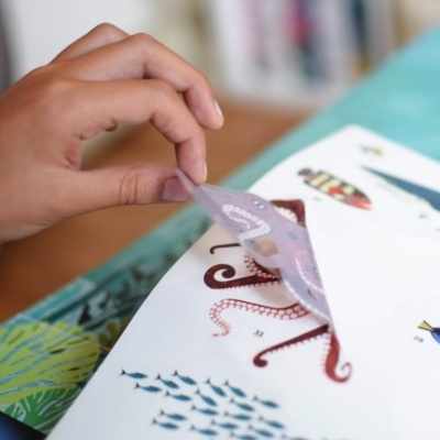 Mão a levantar página transparente com ilustração de polvo sobre folha com imagens marinhas