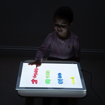 Mesa luminosa branca com números coloridos e criança sentada no escuro