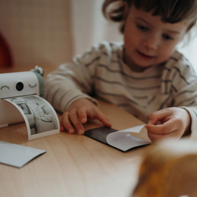 Criança a usar impressora fotográfica pequena e folha preta e branca na mesa