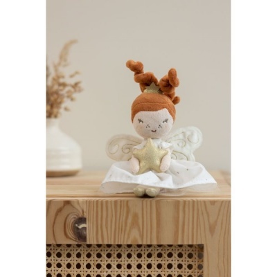 Boneca de tecido com saia branca e asas sentada em móvel de madeira com vaso ao fundo