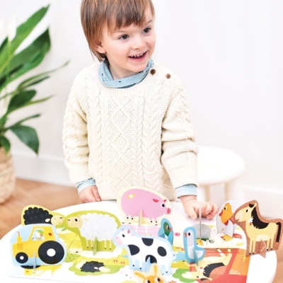 Criança com camisola branca brincando com puzzle de animais de madeira numa mesa branca