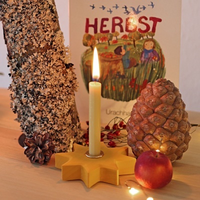 Vela acesa em suporte amarelo, pinhas, maçã, lenha e imagem com texto 'HERBST'