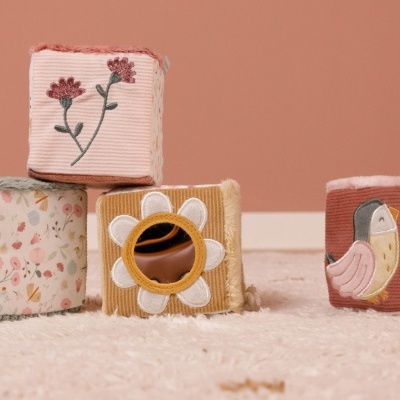 Cubos de tecido para bebé com padrões florais, números e espelho, em ambiente cor-de-rosa e tapete bege.