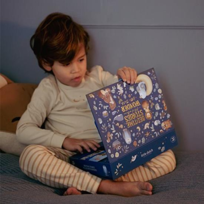 Criança a abrir uma caixa ilustrada azul enquanto está sentada na cama com pijama às riscas.