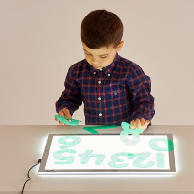 Criança com camisola xadrez azul e vermelho usando peças verdes translúcidas numa mesa iluminada