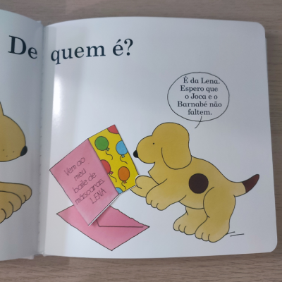 Página ilustrada de livro infantil com cão amarelo e convite cor-de-rosa aberto.