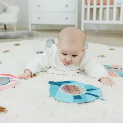 Bebé deitado no tapete a olhar para espelho azul no chão