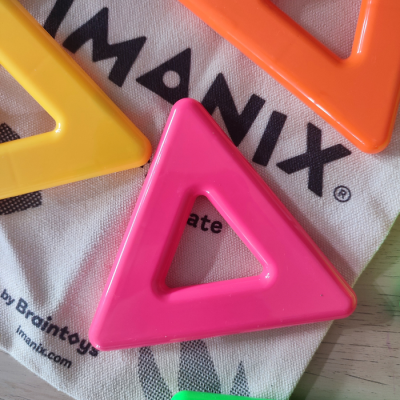 Triângulos plásticos coloridos sobre bolsa de pano branca com texto preto