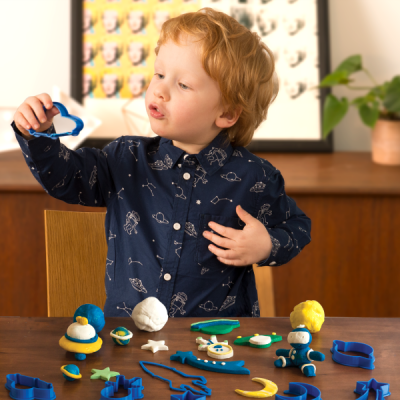 Criança a brincar com argila colorida e formas de cortar numa mesa de madeira