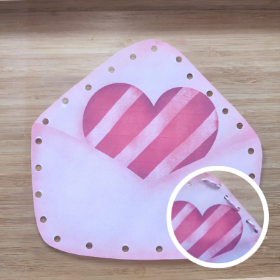 Envelope rosa com buracos e coração riscado em madeira clara