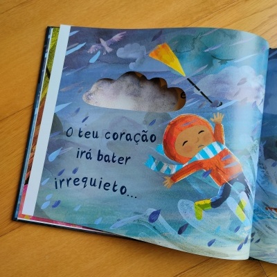 Livro infantil aberto com ilustração de menino na chuva e texto em português