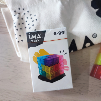 Embalagem com um cubo de peças coloridas e transparentes sobre superfície de madeira clara