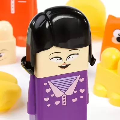 Figura de brinquedo com roupa roxa e cabelo preto, rosto sorridente, rodeada por outras figuras coloridas.