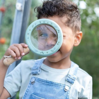 Menino com lupa azul e jardineiras de ganga em ambiente exterior
