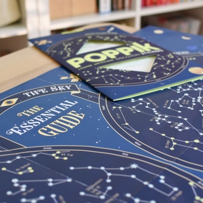 Mapa das estrelas e constelações em fundo azul com embalagem Poppik e estante ao fundo
