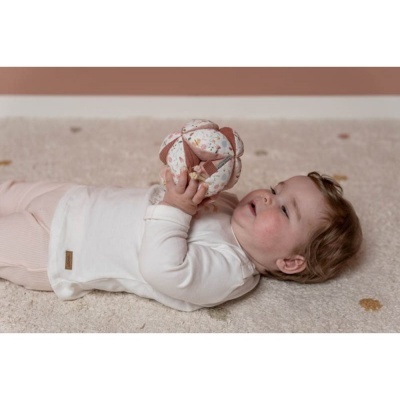 Bebé deitado a segurar bola de tecido com padrões florais