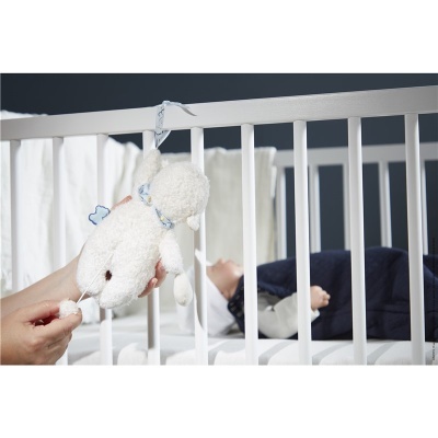 Berço branco com bebé deitado e brinquedo de peluche ovelha pendurado