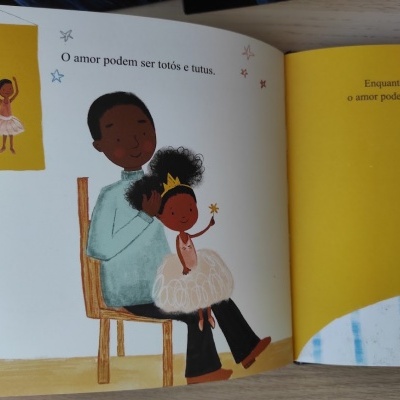 Livro infantil aberto mostrando adulto segurando criança em vestido de bailarina com texto em português