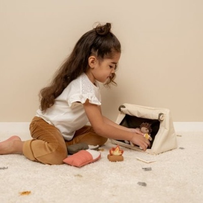 Criança sentada no chão a brincar com brinquedos de madeira junto a uma tenda de tecido