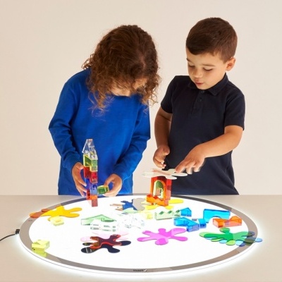 Duas crianças a brincar com peças coloridas numa mesa iluminada