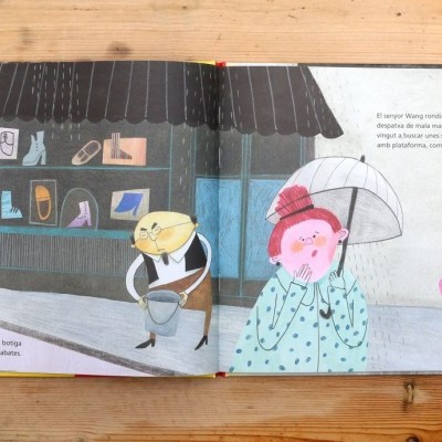 Livro ilustrado aberto mostrando uma cena de rua com personagens e uma loja