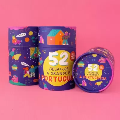 Embalagem cilíndrica roxa com texto '52 DESAFIOS A GRANDE E PORTUGUESA' sobre fundo rosa