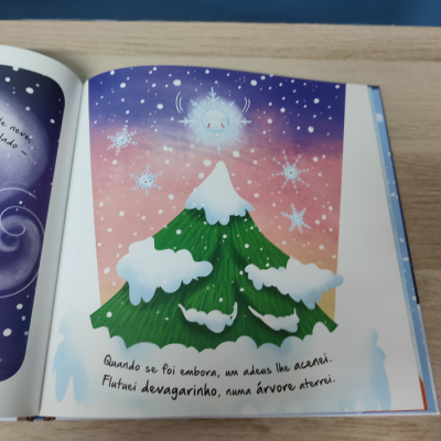 Livro aberto com ilustração de árvore com neve e flocos de neve animados, texto em português.