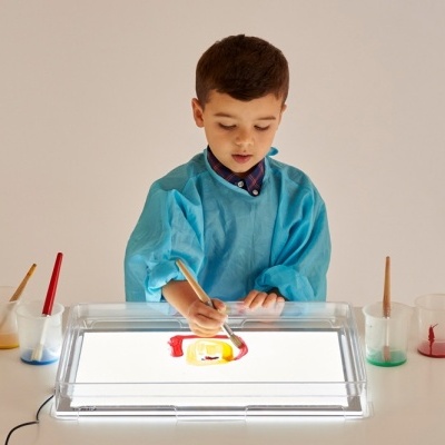 Menino a pintar com tintas coloridas numa mesa iluminada por baixo