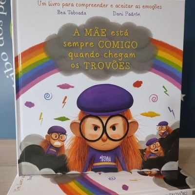 Livro infantil com criança de óculos grandes em capa colorida e arco-íris ao fundo