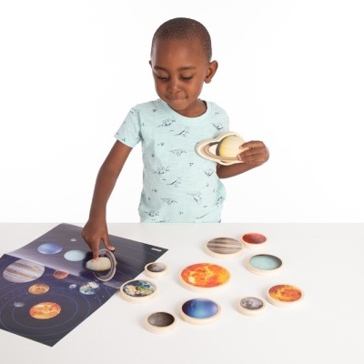 Criança com conjunto do sistema solar em madeira e cartaz educativo