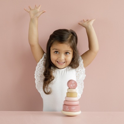 Criança a brincar com brinquedo de empilhar rosa e bege em fundo rosa