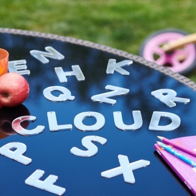 Mesa redonda preta com letras brancas, copo laranja, maçã vermelha, livros cor-de-rosa e bicicleta ao fundo