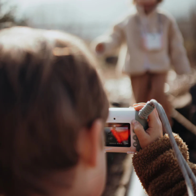 Câmara digital branca na mão de criança a fotografar outra criança desfocada ao ar livre