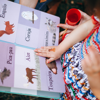 Livro infantil aberto com nomes e desenhos de animais e uma criança a interagir com o livro