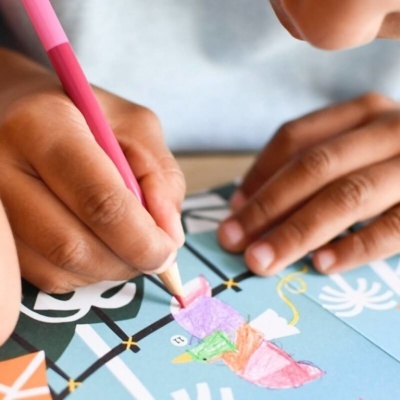 Mãos a colorir desenho com lápis de cor sobre papel azul com padrões variados