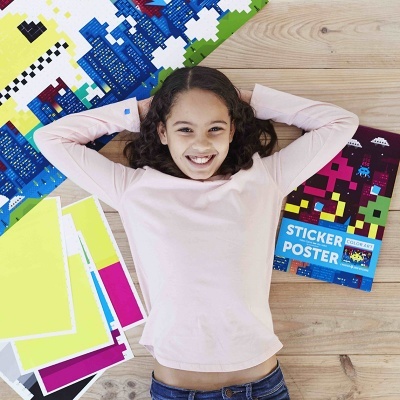 Criança sorridente deitada no chão ao lado de folhas coloridas e um pacote de poster adesivo