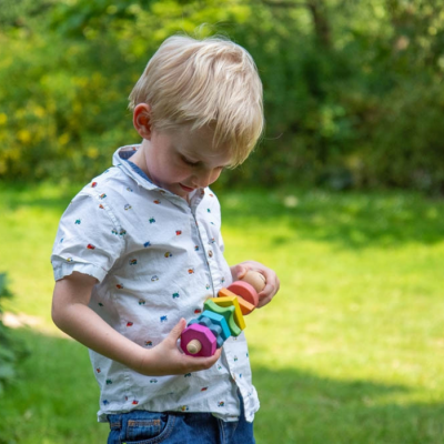 Criança a segurar brinquedo de madeira colorido num jardim verde