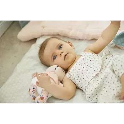 Bebé com macacão branco floral e brinquedo de coelho colorido de tecido numa cama clara