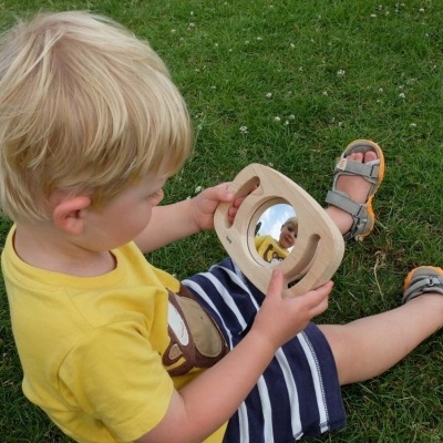 Menino sentado na relva a segurar uma moldura de madeira com espelho redondo