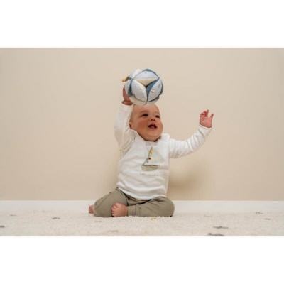 Bebé a brincar com bola macia azul e branca sentado no tapete claro.