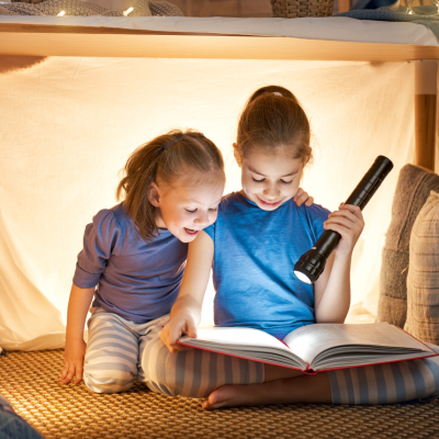 Duas crianças a ler num espaço acolhedor com almofadas e luzes quentes