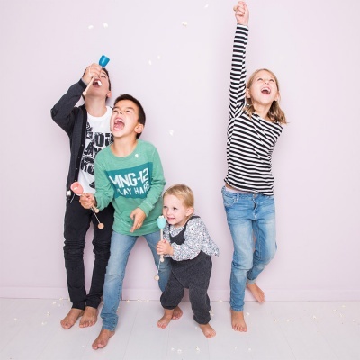 Quatro crianças descalças com apitos coloridos num fundo rosa claro.